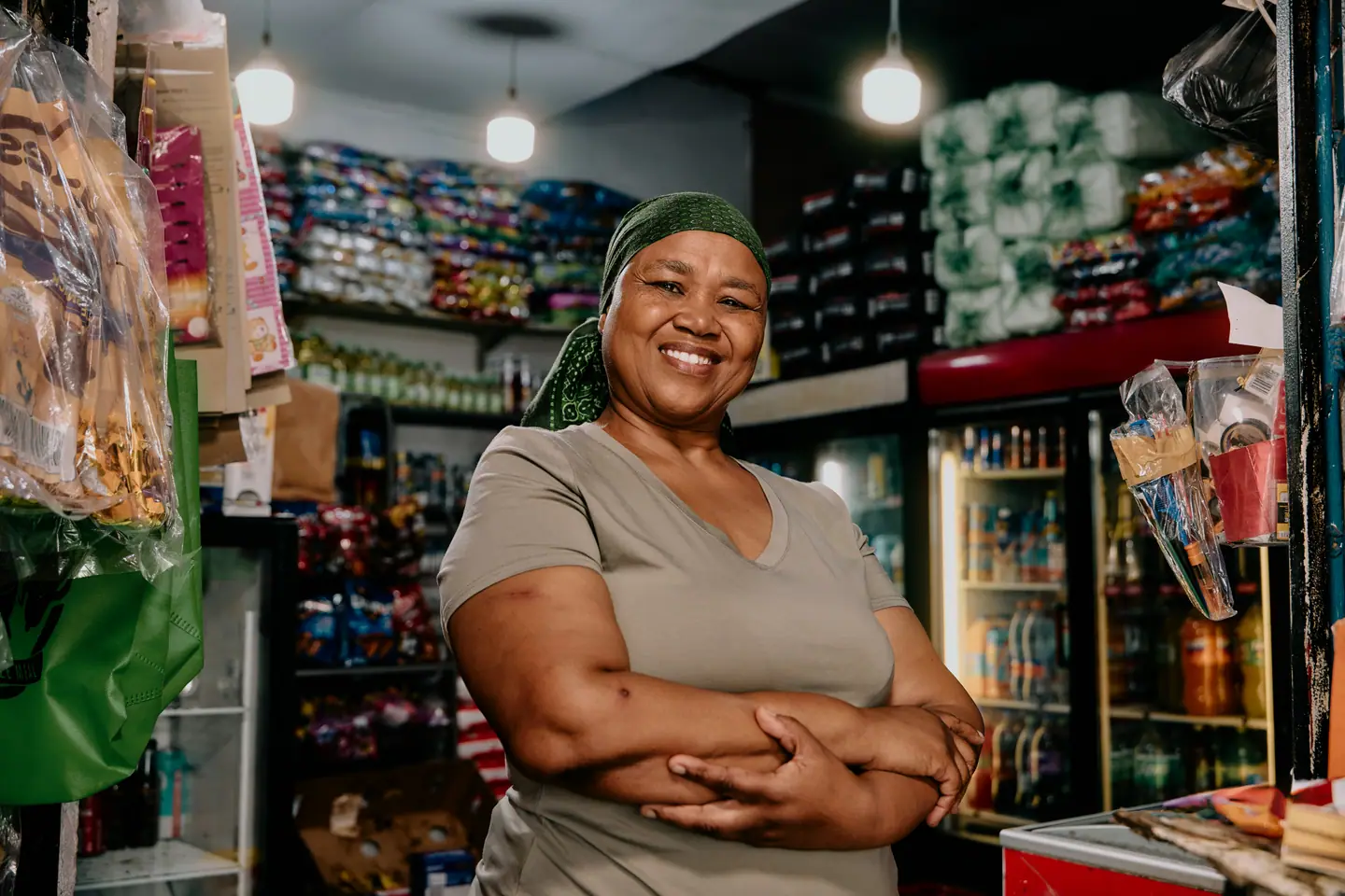 A smiling spaza shop owner with her arms folded